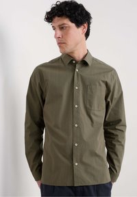 Camisa de manga larga verde oliva con un patrón de cuadros, cuello abotonado y un solo bolsillo en el pecho. La tela parece suave y ligera.