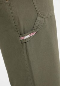 Alyvinės žalios spalvos medvilnės cargo kelnės su šoniniu kišeniu, ant kurio matomas "Guess Jeans" ženklas. Patvari medžiaga ir tiesaus kirpimo dizainas.