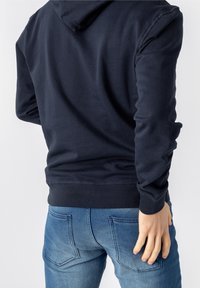 Marinblå hoodie med en mjuk textur, med en känguruficka och ribbade ärmslut. Kombinerad med åtsittande ljusblå jeans.