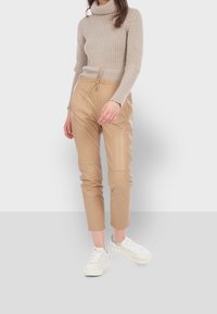 Beige syntetické jogger kalhoty s elastickým pasem a bočními kapsami, v kombinaci se světle pleteným rolákem a bílými teniskami.