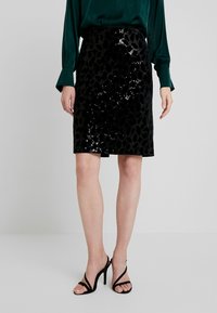 Falda lápiz negra con lentejuelas y un estampado de leopardo, de textura suave y corte hasta la rodilla, combinada con tacones negros con tiras.