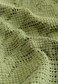 Hele rohelise varjundiga kootud kangas, millel on tekstuuriga, avatud koega muster ning pehmed voldid, mis tekitavad varje ja sügavust.
