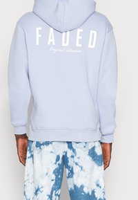 Felpa leggera blu chiaro realizzata in morbido tessuto, con una scritta bianca audace "FADED" sul retro e "Original Sessions" sotto. Jeans tie-dye con effetto strappato.