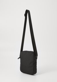 Borsa a spalla nera di forma rettangolare, con tracolla regolabile e tessuto texturizzato. Presenta una chiusura con zip e nessun hardware visibile.
