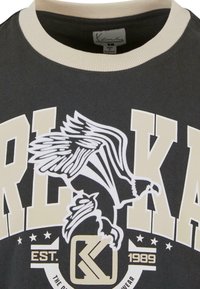 Black T-shirt with a cream ribbed collar, featuring bold cream letters and a detailed eagle graphic in white and cream.