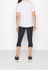 Ljust rosa kortärmad träningsskjorta i kombination med svarta capribyxor, med en figurnära design och mjuk textur, bärs med svarta sportskor.