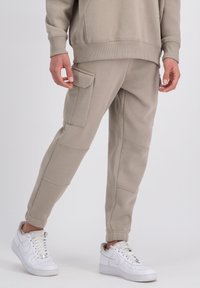 Béžové tepláky s textúrovaným povrchom, bočnou vreckou, rebrovanými manžetami a voľným strihom, skombinované s bielymi teniskami.