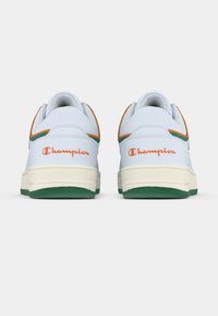 Λευκά αθλητικά παπούτσια με πράσινες και πορτοκαλί λεπτομέρειες, δερμάτινο υλικό και υφασμένες λαστιχένιες σόλες. Το λογότυπο "Champion" εμφανίζεται στη φτέρνα.