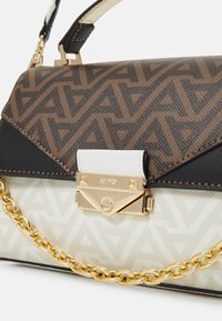 Sac à main avec un motif géométrique marron et des accents en cuir noir. Présente une chaîne en or et un fermoir métallique sur un fond crème.