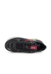 Zapatilla deportiva negra con acentos rojos, con un upper texturizado, cordones resistentes y detalles reflectantes. La suela tiene un diseño multicolor.