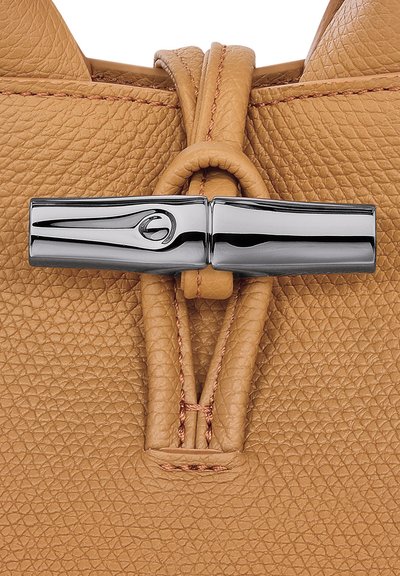 Tan pebbled leather bag with a polished silver hardware clasp, featuring braided detailing and a smooth finish. Textured surface is prominent.