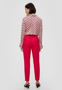 Blouse à manches longues avec un motif en chevrons rose et noir, associée à un pantalon ajusté rose vif. Tissu lisse, design cintré, détail arrière subtil.