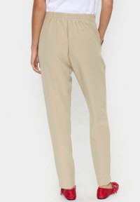 Beige, lätta byxor med elastisk midja, raka ben och sidofickor, kombinerade med röda platta skor.