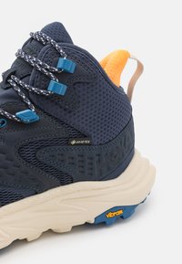 Námořnická turistická obuv s prodyšnou síťovinou, modrým šněrováním a oranžovým patním poutkem. Obsahuje štítek Gore-Tex a vibramovou podrážku pro dobrou přilnavost.