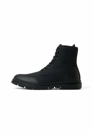 Black ankle boots made of rubber with a smooth finish, featuring a lace-up front, padded collar, and sturdy textured sole.