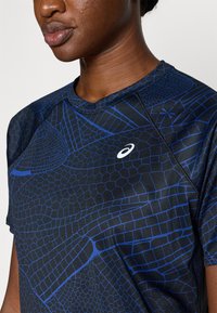 Černé sportovní tričko s krátkým rukávem, zdobené modrým geometrickým vzorem, kulatým výstřihem a bílým logem na hrudi. Měkká, přiléhavá textura.