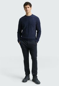 Marineblauer Strickpullover mit strukturiertem Muster, Rundhalsausschnitt und langen Ärmeln, kombiniert mit dunklen Hosen und schwarzen Sneakern.