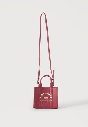 Petit sac à main rouge texturé avec longue bandoulière et poignées, présentant un texte blanc Karl Lagerfeld Paris et une adresse sur le devant.