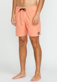 Pfirsichfarbene Schwimmshorts mit einem elastischen Bund, schwarzem Kordelzug und Seitentasche. Mit einem runden Logo auf dem linken Oberschenkel.