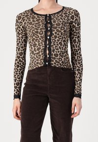 Cardigan con stampa leopardata e maniche lunghe, rifinito con dettagli in pizzo nero e chiusura a bottoni. Abbinato a pantaloni in velluto a coste marroni.