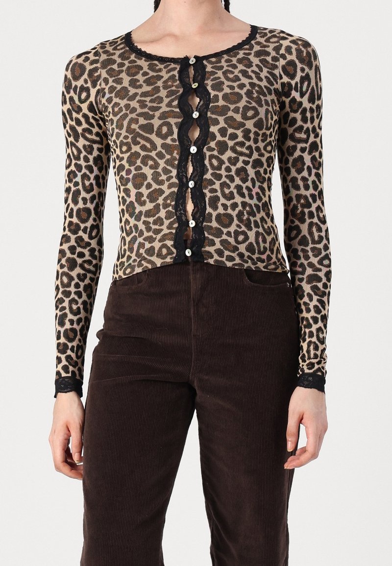 Cardigan con stampa leopardata e maniche lunghe, rifinito con dettagli in pizzo nero e chiusura a bottoni. Abbinato a pantaloni in velluto a coste marroni.