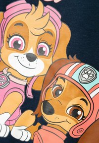 Due cani cartoni animati che indossano attrezzature rosa; uno ha un casco rosa con un distintivo a forma di zampa, e l'altro ha occhiali rosa e un collare.