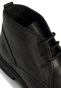 Bottine en cuir noir à la surface texturée, fermeture à lacets et coutures renforcées. Dispose d'une semelle en caoutchouc noir basse.