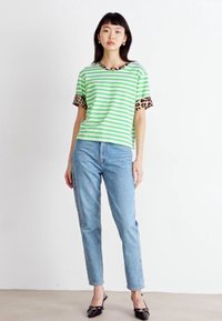 Gestreept groen en wit t-shirt met korte mouwen van luipaardprint, gecombineerd met lichtblauwe jeans en zwarte puntige flats.