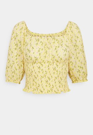 Gelbe kürzere Bluse mit kleinem Blumenmuster, weiten Dreiviertelärmeln, smock-tailliert und mit quadratischem Ausschnitt.