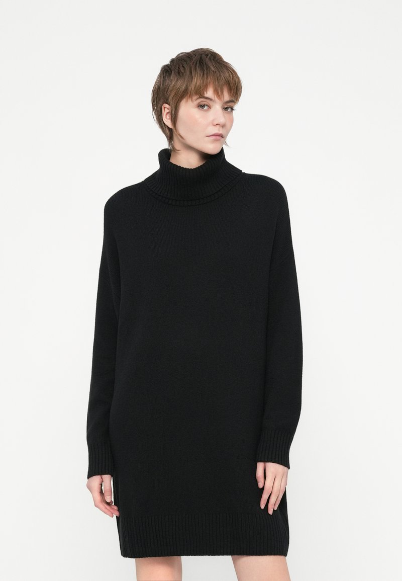 Crna oversized haljina s turtleneck izrezom, pletiva, dugi rukavi, rebrasti rukavi i donji rub, opušteni kroj, mekana tkanina.