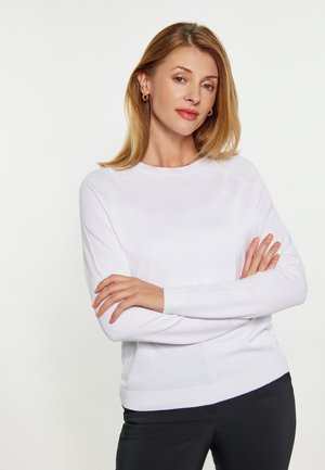 Witte lange mouw top met een ronde hals en ribgebreide manchetten, gecombineerd met zwarte broek. De stof lijkt zacht en soepel, met een eenvoudig ontwerp.