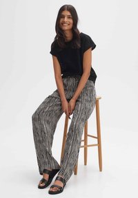 Zwart gehaakt topje met korte mouwen en een losse pasvorm, gecombineerd met zwart-wit gestreepte wijde broek. Zwarte slip-on sandalen.