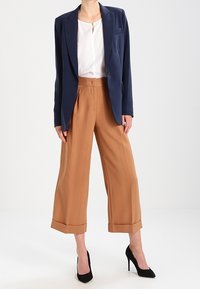 Námořnický blejzr s jedním knoflíkem, kombinovaný s béžovými širokými kalhotami s manžetou. Černé vysoké podpatky doplňují outfit.