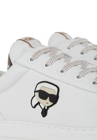 Sneakers bianchi in pelle con accenti marroni, dotati di un logo a cartone sul lato, lacci texturizzati e occhielli rotondi per l'inserimento dei lacci.