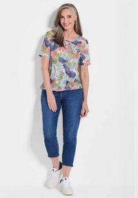 Korte mouw met bloemenprint in pastelkleuren, met een ronde halslijn en een relaxte pasvorm, gecombineerd met blauwe cropped jeans en witte sneakers.