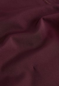 Burgunderroter Stoff mit glatter Textur, der sanfte Falten und einen leichten Glanz zeigt. Keine Muster oder sichtbaren Beschläge, wodurch die Einfachheit betont wird.