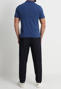 Polo bleu marine à manches courtes, en tissu maille doux, associé à un pantalon noir et des baskets blanches.