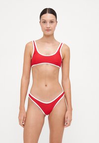 Červený bikiny set obsahujúci top s okrúhlym výstrihom a širokými ramienkami a zodpovedajúce nízko vystúpené spodné diely, obidva s bielym lemovaním. Hladká textúra.