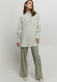 Lockere, gestreifte Button-up-Bluse aus hellgrünem und weißem Stoff mit zwei Brusttaschen, kombiniert mit hellgrünen, weiten Hosen.