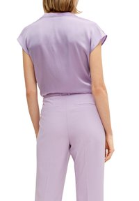 Lilarosa blus med uppvikta ärmar, tillverkad av mjukt tyg, kombinerad med matchande lilarosa byxor med bakfickor och skräddarsydd passform.