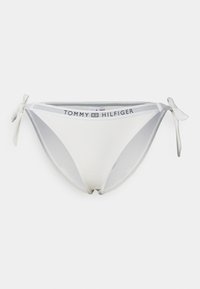 Hvit bikinitruse med teksturert stoff, med snører på sidene og en merket linning med "TOMMY HILFIGER"-logo.