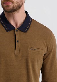 Braun strukturierter Poloshirt mit einem marineblauen Kragen und passenden Akzenten. Verfügt über zwei Knöpfe und eine kleine Brusttasche mit Branding.