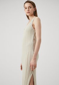 Pletené maxi šaty v off-white farbe s textúrovaným vzorom, hlbokým výstrihom a bočnými rozparokmi pre pohodlný pohyb.