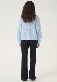 Tekstureeritud helesinine kootud sviiter vaba lõikega, millel on rombikujuline muster, koos tumedate flokeeritud teksade ja kontsakingadega.