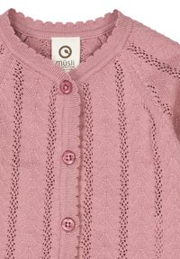 Vaaleanpunainen neulecardigan, jossa on aaltoileva kaulus ja pitsikuvio. Edessä on kaksi pyöreää vaaleanpunaista nappia suljentaa varten.
