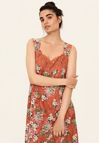 Bloemjurk in roestkleur met kantaccenten, voorzien van brede banden en een getailleerd lijfje. Het patroon bevat gekleurde bloemen op gestructureerde stof.