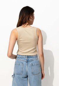 Débardeur beige à côtes avec un col rond, associé à un short en jean bleu clair taille haute, dotée de poches arrières et d'une coupe relax. 