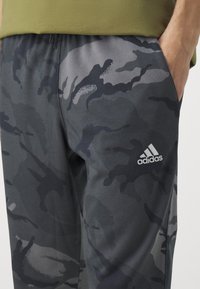 Mörkgrå camouflagebyxor av mjukt material, elastisk midja och vit Adidas-logotyp på vänster lår.