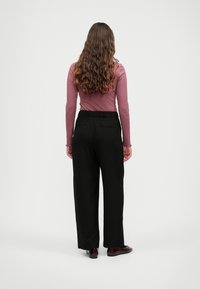 Pantalons large noirs avec une taille à cordon de serrage, associés à un top ajusté à manches longues de couleur rose poussiéreux. Le tissu semble lisse et léger.
