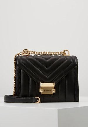 Sac à main en cuir matelassé noir avec bandoulière chaîne dorée et fermoir doré gravé du logo Michael Kors, présenté sur une surface blanche.